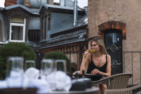Junge Frau sitzt auf der Dachterrasse und trinkt eine Tasse Kaffee - KKAF02630