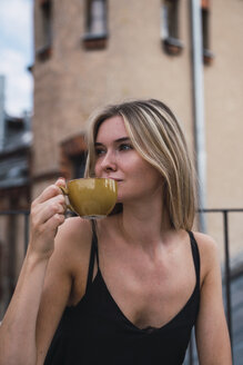 Porträt einer jungen Frau, die auf dem Balkon eine Tasse Kaffee trinkt - KKAF02633