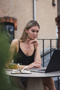 Porträt einer jungen Frau, die auf einer Dachterrasse sitzt und einen Laptop benutzt - KKAF02637