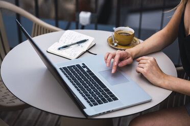 Junge Frau sitzt auf dem Balkon und arbeitet am Laptop, Teilansicht - KKAF02638