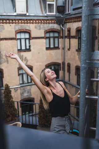 Glückliche junge Frau auf Balkon, die eine Feuerleiter erklimmt, lizenzfreies Stockfoto