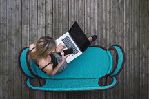 Young woman sitting on turquoise couch on terrace using laptop, top view -  a Royalty Free Stock Photo from Photocase