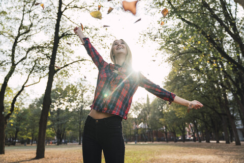 Happy young woman throwing autumn leaves in the air stock photo