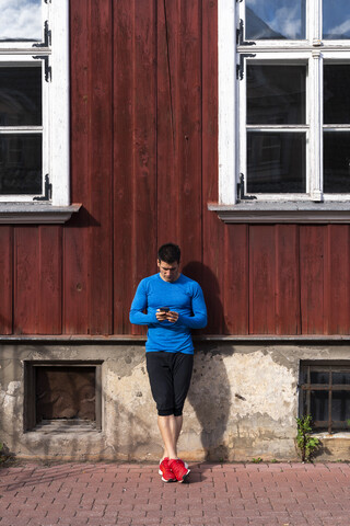 Sportler lehnt an einer Hauswand und benutzt ein Mobiltelefon, lizenzfreies Stockfoto