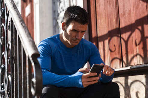 Sportler sitzt auf der vorderen Treppe und benutzt ein Mobiltelefon - KKAF02709