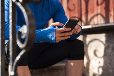 Nahaufnahme eines Sportlers, der auf der vorderen Treppe sitzt und ein Mobiltelefon benutzt - KKAF02710