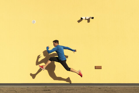 Sportlicher Mann trainiert an gelber Wand mit CCTV-Kamera, lizenzfreies Stockfoto