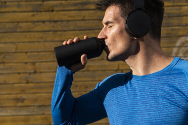 Athlete with headphones drinking from drinking bottle - KKAF02730