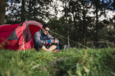 Mann zeltet in Estland, sitzt im Zelt und benutzt sein Smartphone - KKA02748