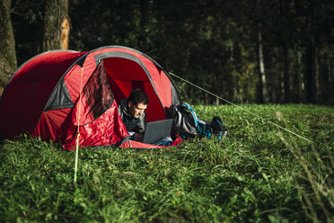 Man camping in Estonia, sitting in his tent, using laptop - KKA02758