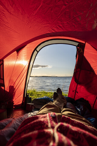 Mann zeltet in Estland und beobachtet den Sonnenuntergang im Zelt liegend, lizenzfreies Stockfoto