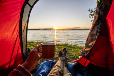 Mann zeltet in Estland und beobachtet den Sonnenuntergang im Zelt liegend - KKA02778