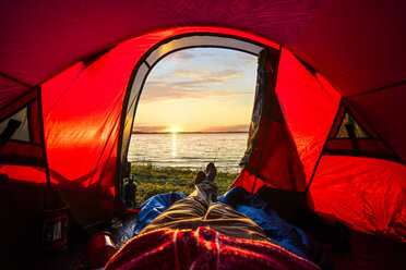 Mann zeltet in Estland und beobachtet den Sonnenuntergang im Zelt liegend - KKA02779