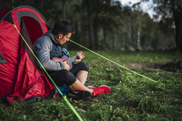 Mann zeltet in Estland, sitzt in seinem Zelt und spielt Ukulele - KKA02780
