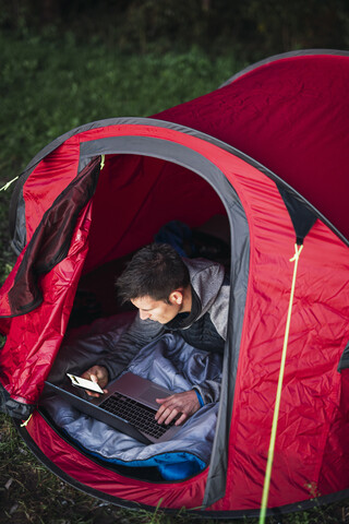 Mann zeltet in Estland, sitzt im Zelt und benutzt einen Laptop, lizenzfreies Stockfoto