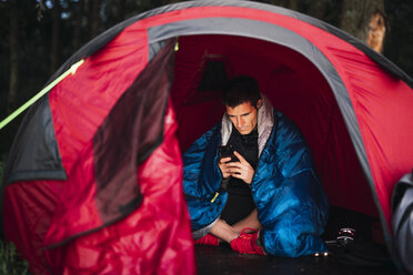 Mann zeltet in Estland, sitzt in seinem Zelt und benutzt sein Smartphone - KKA02794