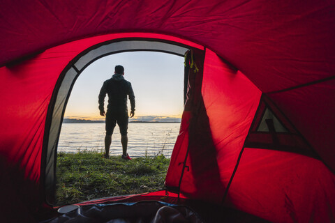 Man camping in Estonia, standing in front of tent, watching sunset stock photo