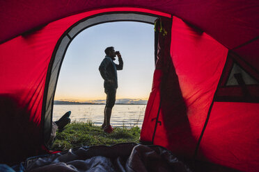 Man camping in Estonia, standing in front of tent, watching sunset - KKA02797