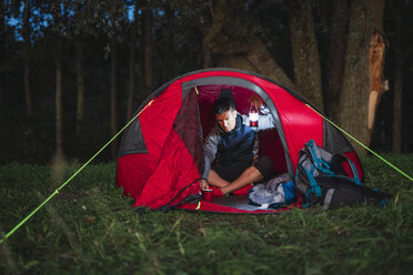 Man camping in Estonia, sitting in his tent, holding latern - KKA02798