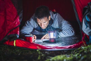 Man camping in Estonia, drawing in his sketchbook at night - KKA02803