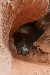 Junger Mann sitzt in einer Höhle und schaut durch ein Fernglas - AFVF01863