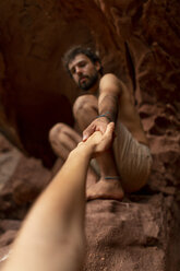 Junger Mann sitzt in einer Höhle und greift nach der Hand einer Frau - AFVF01870