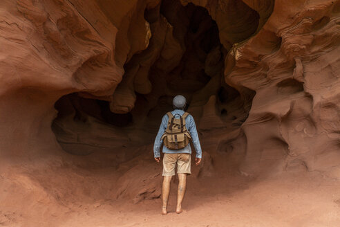 Young man with backpack, looking at cave, rear view - AFVF01875