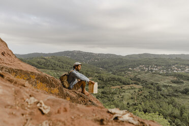 Junger Mann mit Rucksack, auf einem Berg sitzend, mit Blick auf die Aussicht - AFVF01878