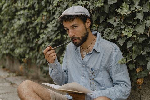 Young man smoking pipe, reading a book stock photo