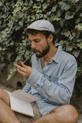 Young man smoking pipe, reading a book - AFVF01881