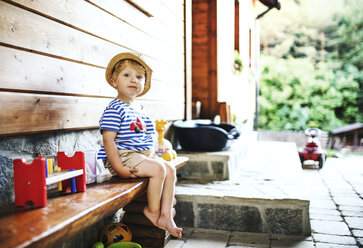 Porträt eines Kleinkindes, das auf einer Bank vor einem Haus sitzt - HAPF02797