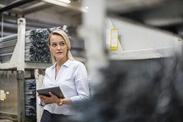 Blond woman holding tablet in high rack warehouse - DIGF05417