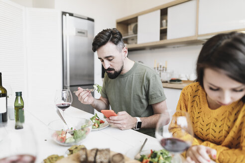 Mann prüft Nachrichten auf dem Mobiltelefon, während er mit seiner Freundin zu Hause zu Mittag isst - KMKF00598