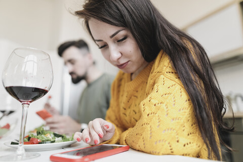 Junge Frau überprüft ihr Smartphone beim Mittagessen zu Hause, lizenzfreies Stockfoto