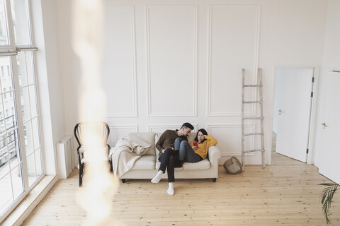 Ehepaar sitzt auf der Couch im Wohnzimmer des neuen Hauses und schaut auf das Handy, lizenzfreies Stockfoto