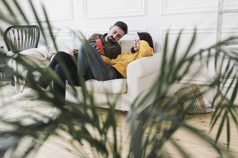 Ehepaar sitzt auf der Couch im Wohnzimmer des neuen Hauses und schaut auf das Handy, lizenzfreies Stockfoto