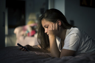 Teenage girl using smart phone while lying on bed at home - CAVF50588