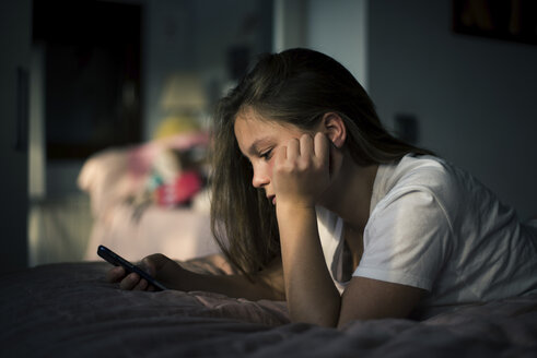 Teenager-Mädchen benutzt ihr Smartphone, während sie zu Hause auf dem Bett liegt - CAVF50588