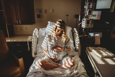 Pregnant woman touching stomach while sitting on bed in hospital - CAVF50590