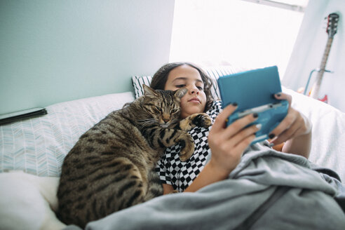Hohe Winkel Ansicht des Mädchens spielen Videospiel, während mit Katze auf dem Bett zu Hause liegen - CAVF50592