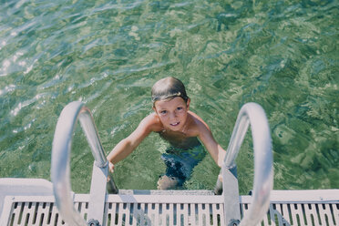 Hochwinkliges Porträt eines Jungen ohne Hemd, der sich auf einer Leiter im See bewegt - CAVF50630