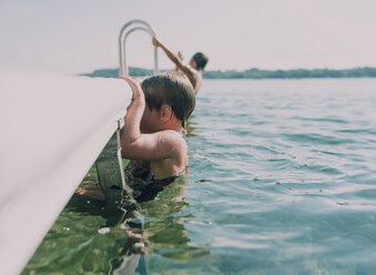 Siblings balancing on pier while swimming in lake against sky - CAVF50631