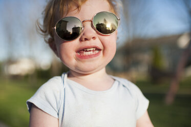 Close-up portrait of cute happy baby boy wearing sunglasses while standing in yard - CAVF50633