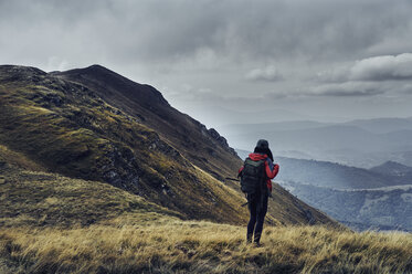 Rear view of female hiker with backpack standing on Balkan Mountains against cloudy sky - CAVF50641