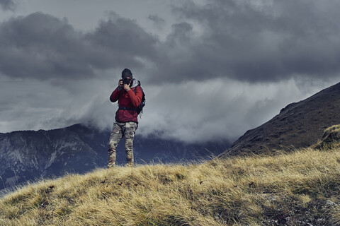 Männlicher Wanderer, der auf einem Berg stehend gegen einen bewölkten Himmel fotografiert, lizenzfreies Stockfoto