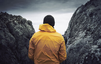 Rear view of man standing by rock formations against cloudy sky during winter - CAVF50646