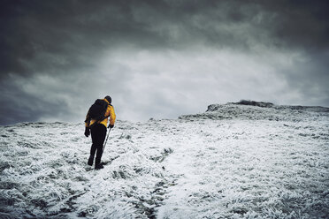 Rückansicht eines männlichen Wanderers, der auf einem schneebedeckten Berg gegen einen bewölkten Himmel läuft - CAVF50647