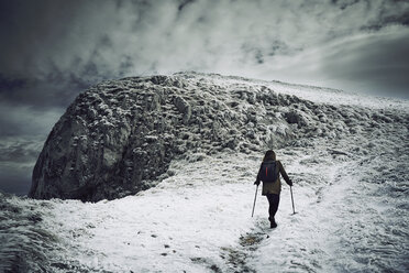 Rückansicht einer Wanderin, die auf einem schneebedeckten Berg gegen einen bewölkten Himmel wandert - CAVF50648