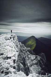 Blick auf eine Frau in mittlerer Entfernung auf einem schneebedeckten Berg vor einem bewölkten Himmel - CAVF50649