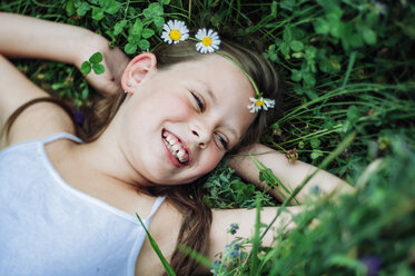 High angle view of happy girl looking away while lying on field amidst plants at park - CAVF50654